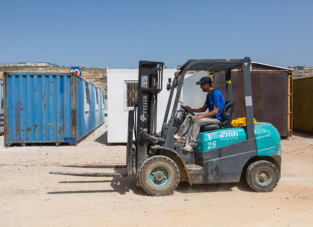 עובד מפעיל מלגזה לשינוע מכולות אחסון באתר עבודה – פתרון לוגיסטי יעיל לניהול ותפעול מכולות, מבנים יבילים ויחידות אחסון.